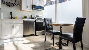 Una cocina moderna con gabinetes blancos, electrodomésticos de acero inoxidable y un comedor con sillas negras.