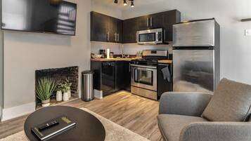 Een moderne keuken met donkere kastjes, roestvrijstalen apparatuur en een flatscreen televisie boven de werkruimte.