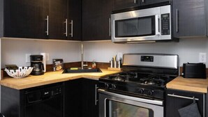 Une cuisine compacte avec des meubles de couleur sombre, un four à micro-ondes en acier inoxydable, une cuisinière à gaz et un four encastré.