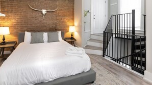 Une chambre à coucher avec un grand lit, un mur en briques, une décoration représentant une tête de taureau, un escalier et une porte.