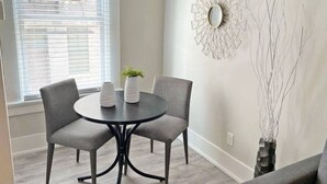 Un coin repas comprenant une table ronde et deux chaises, un élément décoratif mural et un grand vase orné de branches.