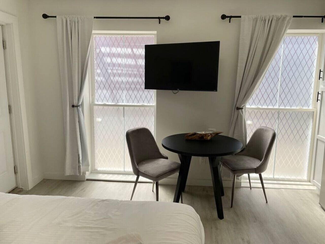 A hotel room with a bed, two chairs, a table, a TV, and large windows with curtains.