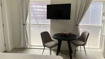 A hotel room with a bed, two chairs, a table, a TV, and large windows with curtains.