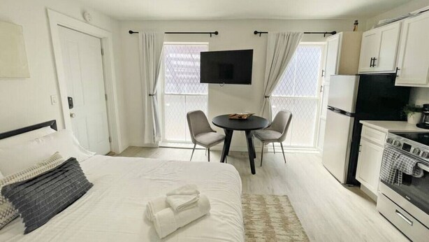 Ett hotellrum med en säng, ett matbord med stolar, en TV, ett kylskåp och en spis.