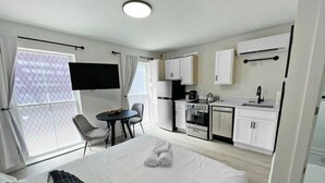 Ett modernt hotellrum med en stor säng, ett skrivbord, ett litet kök och en TV.