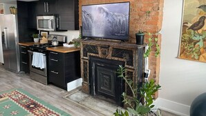 A modern kitchen with a stone fireplace, a flat-screen TV, and a refrigerator.