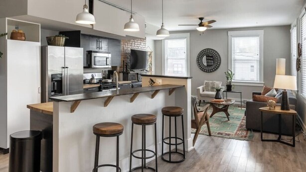 A modern kitchen with a central island, bar stools, and a dining area with a sofa and coffee table.