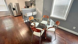 Een moderne keuken met roestvrijstalen apparatuur, een eethoek met een glazen tafel en metalen stoelen, en een groot raam met zonwering.