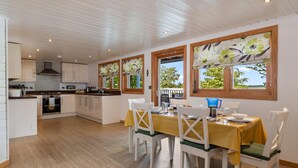 A modern kitchen with white cabinets, a central island, and a dining area with a yellow tablecloth and white chairs. - The Bluebell - Luxury Lodge With Hot Tub (Tenby)