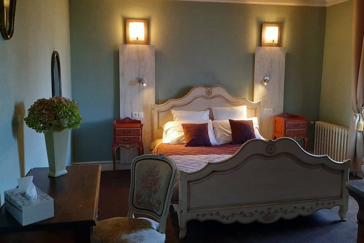 Ein Schlafzimmer mit einem großen Bett, zwei Nachttischen, einem Sessel, einer Heizung und einem Wandspiegel.