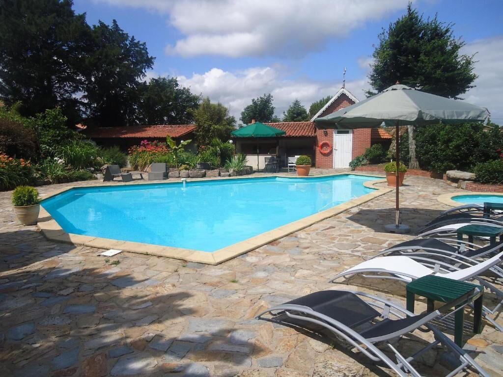 A swimming pool with lounge chairs and umbrellas, surrounded by stone tiles and greenery.
