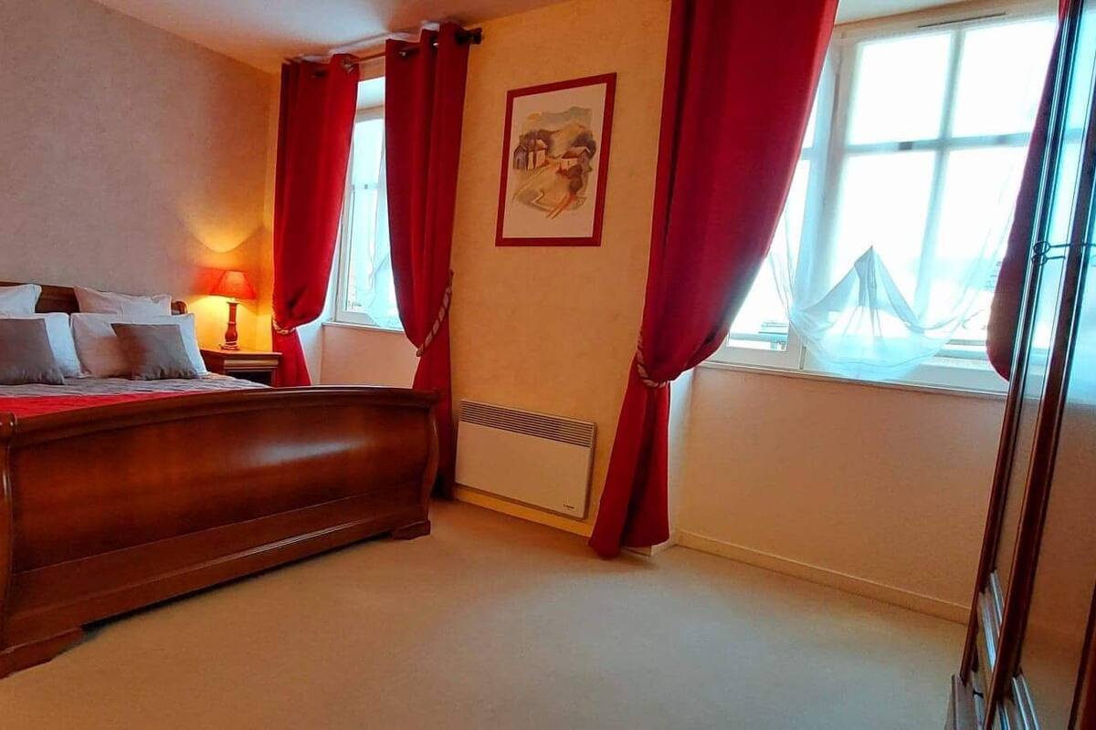 Ein Schlafzimmer mit einem hölzernen Bett, roten Vorhängen, einem Nachttisch mit Lampe und einem Fenster mit Blick.
