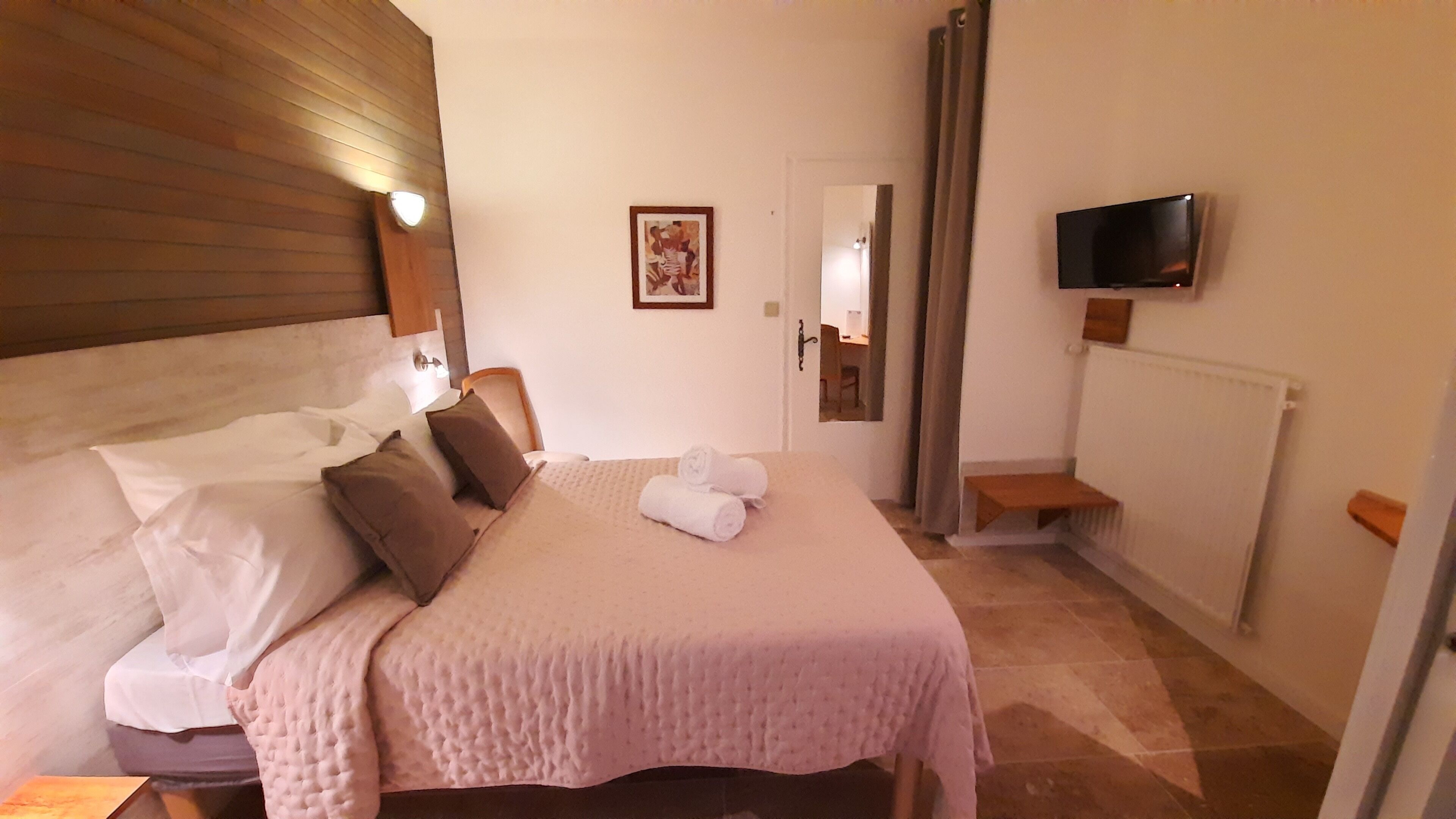 A hotel room with a bed, pillows, a TV, a door, and a window.