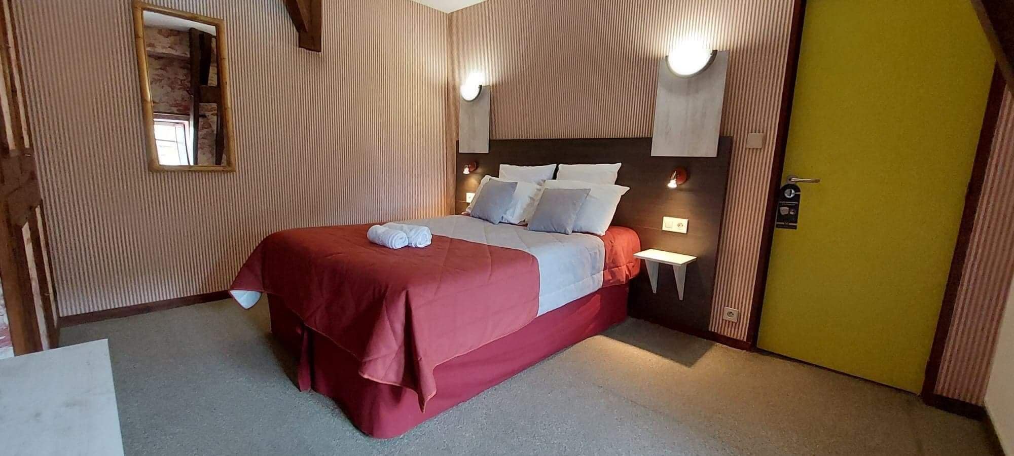 Una habitación de hotel con cama, mesitas de noche, un espejo y una puerta.