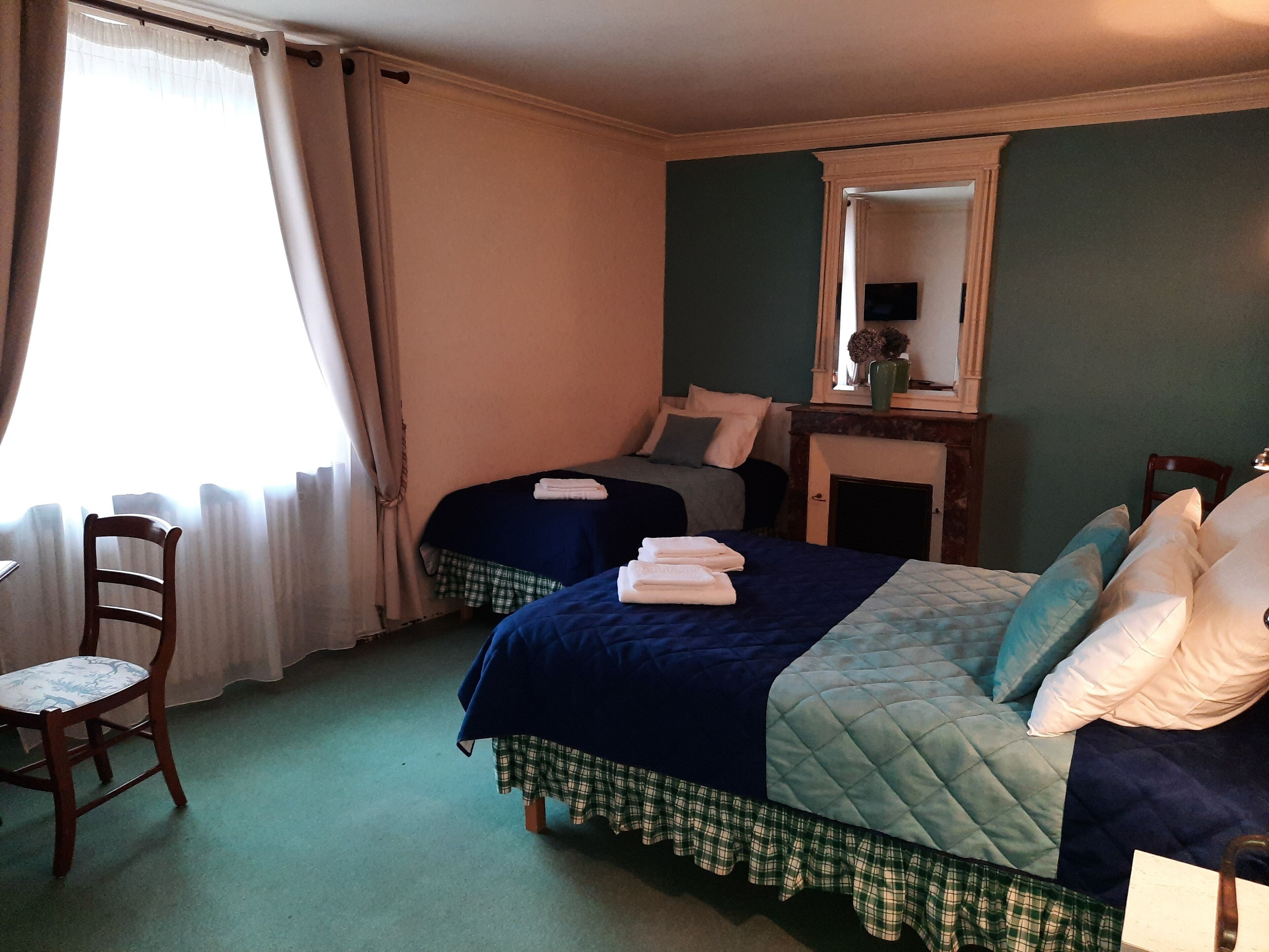 Ett hotellrum med två sängar, en stol, en spegel och ett fönster med gardiner.