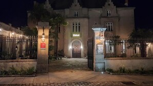 A historic building with a central entrance, a sign indicating it is a hotel, and a gated driveway.