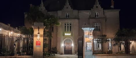 En historisk bygning med en midterindgang, et skilt der angiver at det er et hotel, samt en port med hegnet indkørsel.