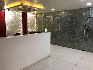 Un área de recepción con diseño moderno, que presenta una pared con textura, un mostrador blanco y una unidad de aire acondicionado instalada en el techo.