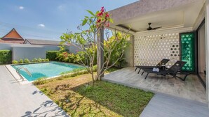 Zona de piscina exterior moderna amb una piscina blava cristal·lina, un arbre petit amb flors roses i dues gandules.
