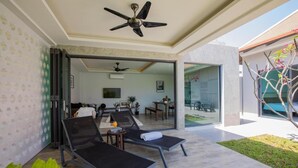 Zona d'estar exterior moderna amb dues gandules, un ventilador de sostre i una porta de vidre que dona a una zona de menjador.