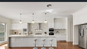 Une cuisine moderne avec des meubles blancs, des appareils en acier inoxydable et un îlot central doté de tabourets de bar.
