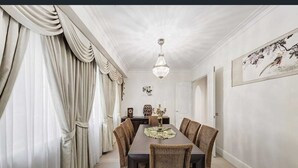 Une salle à manger avec une longue table, des chaises en osier, un lustre et un tableau encadré au mur.
