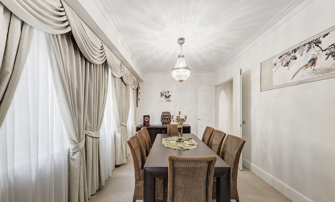 A dining room with a long table, wicker chairs, a chandelier, and a framed picture on the wall.
