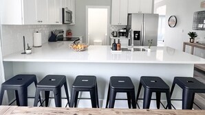 Uma cozinha moderna com armários brancos, uma ilha central e banquetas pretas.