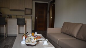 A modern living room with a sofa, a dining table set with breakfast items, and a kitchen area in the background. - byblos palms hotel (Blat)
