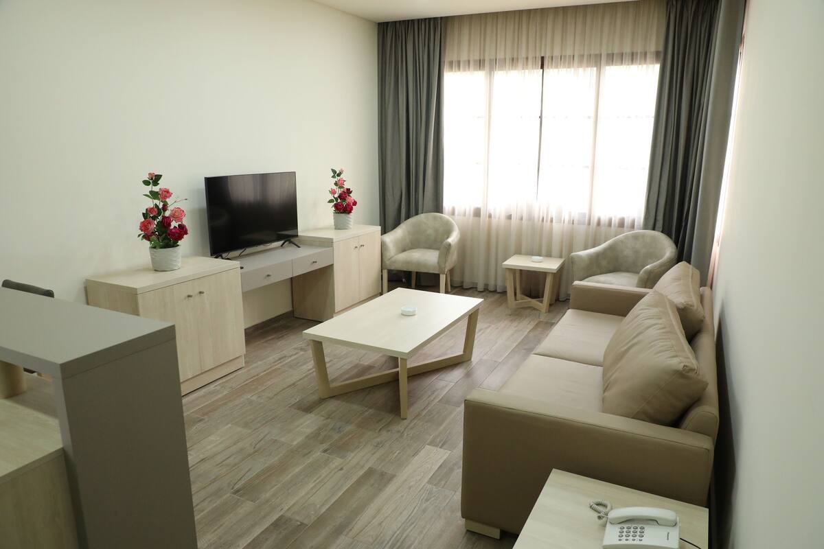 A modern living room with a sofa, two armchairs, a coffee table, a TV, a small table with a phone, and a cabinet.
