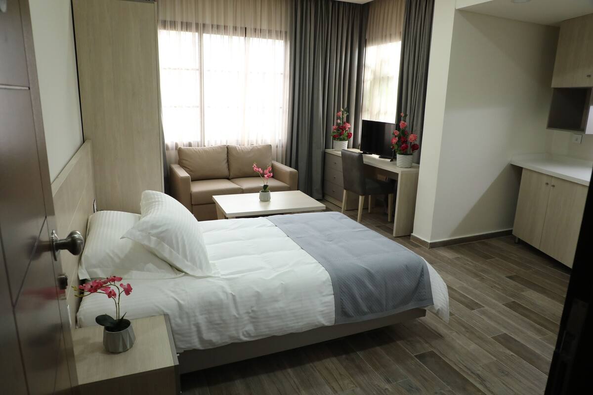 A modern hotel room with a bed, a sofa, a desk, and a TV.