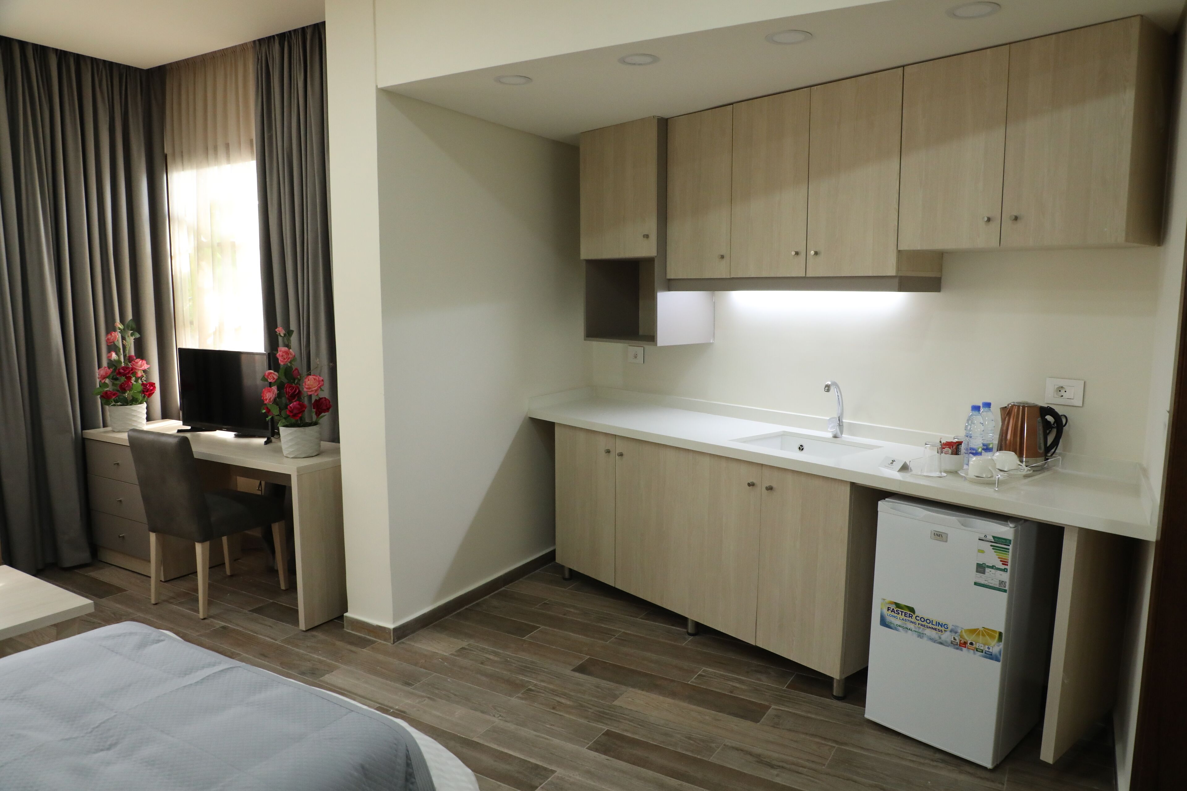 Una habitación de hotel compacta con kitchenette, una cama, un escritorio con computadora y televisión.