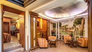 Um lobby com piso de mármore, poltronas listradas, uma mesa de centro e um mural com paisagem.