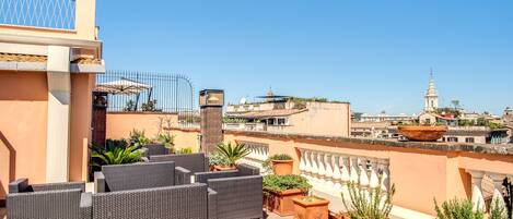 Una terraza en la azotea con mobiliario de mimbre, plantas en macetas y vistas a la ciudad.