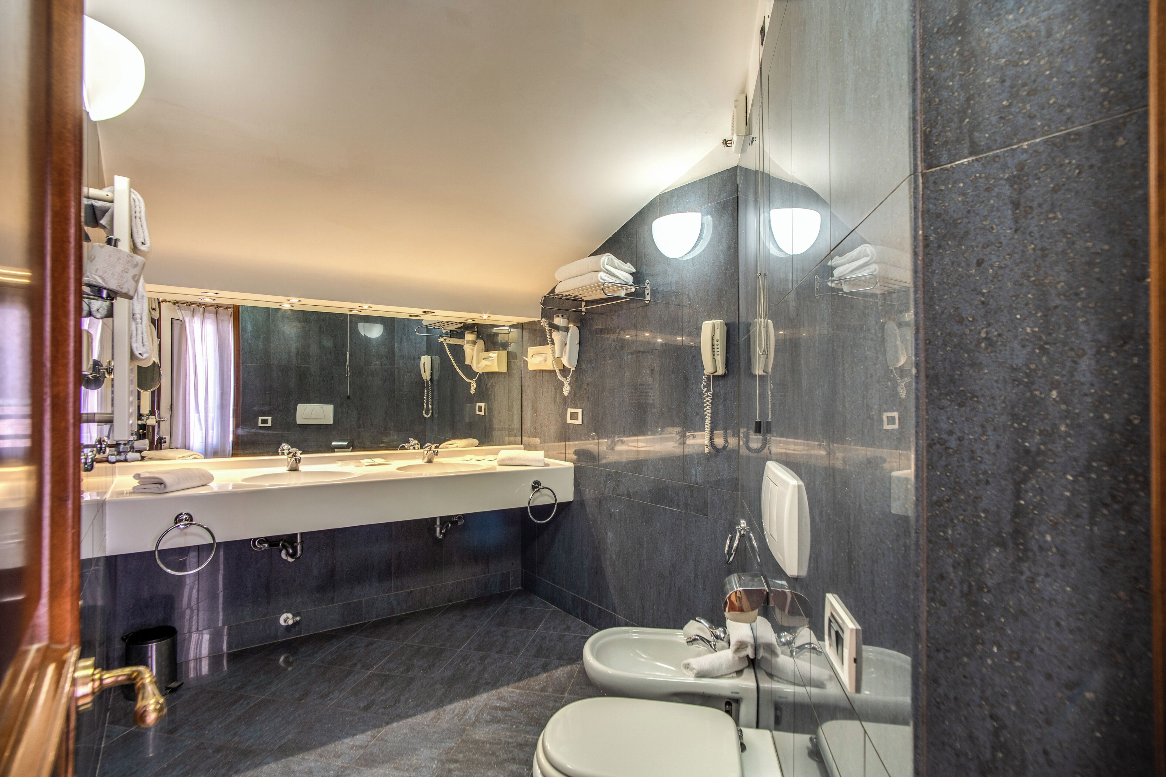 A modern bathroom with a large mirror, dual sinks, a toilet, and a shower area.