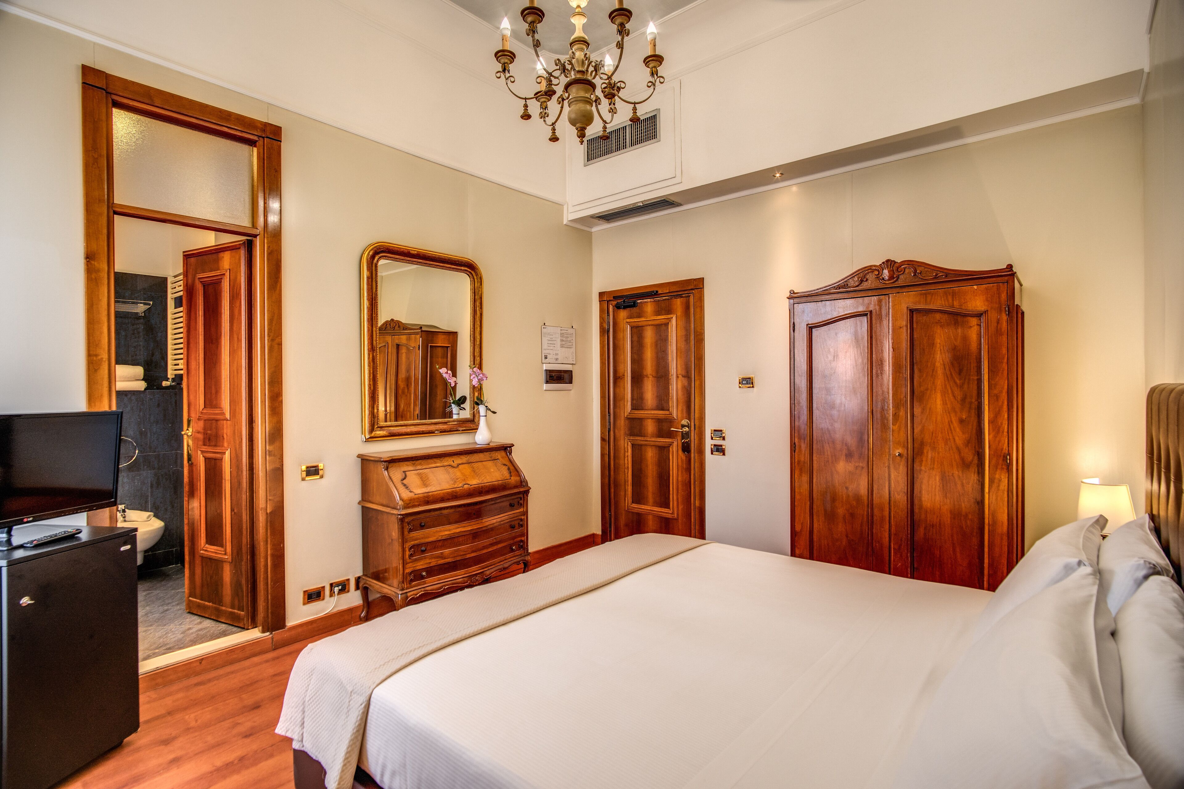A hotel room with a large bed, wooden wardrobe, a dresser, a television, and a mirror.