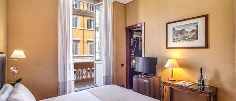 A hotel room with a bed, a television, a desk with a lamp, a framed picture on the wall, and a view of the outside balcony.