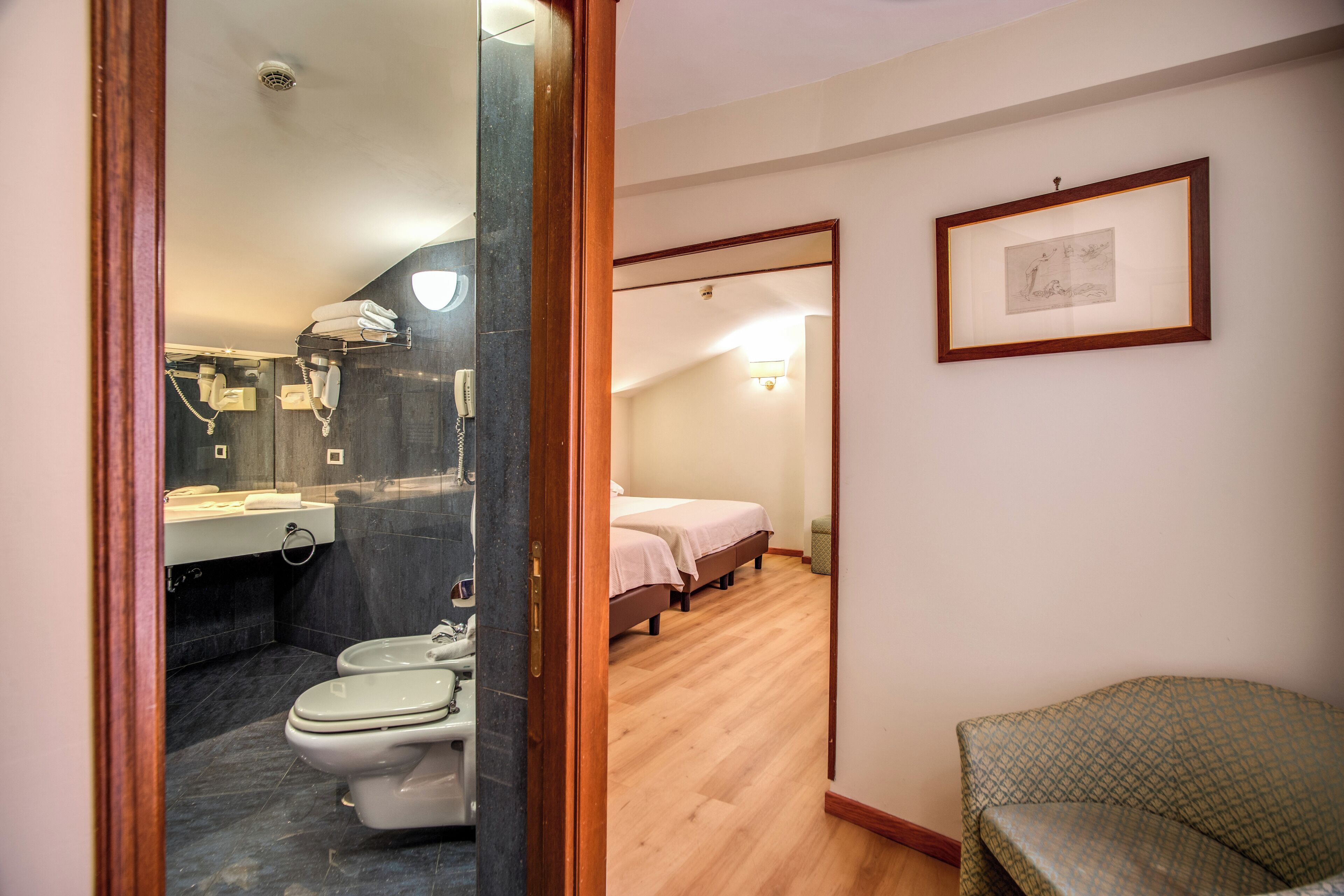 A hotel room with a bathroom, a bed, and a chair.