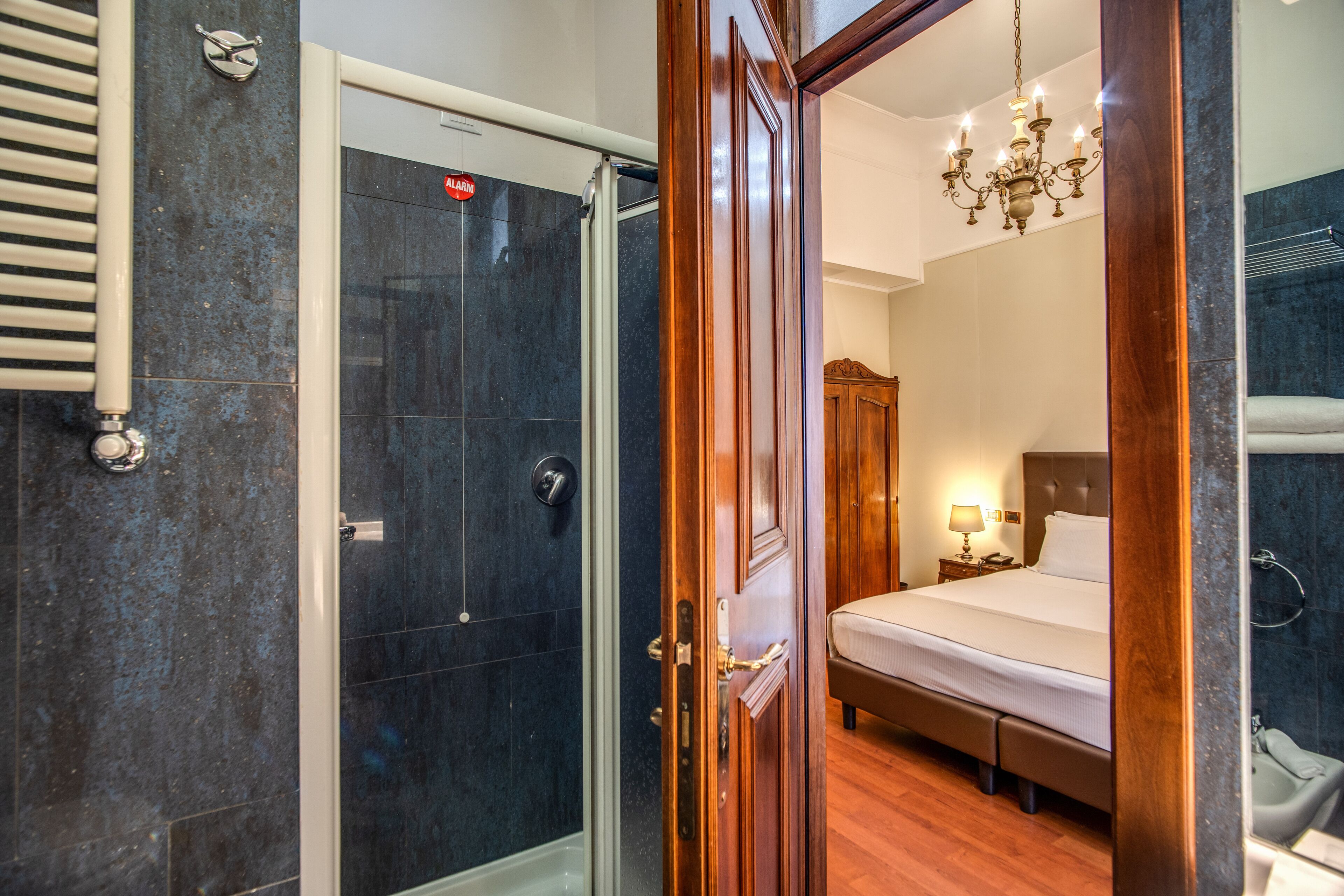 A hotel room with a shower, a bed, a nightstand, and a chandelier.