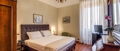 A hotel room with a large bed, a chandelier, a television, and a desk with a lamp.