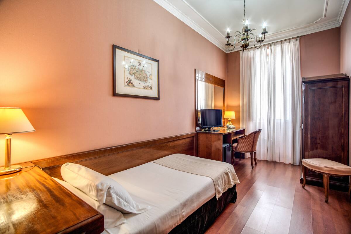 A hotel room with a bed, desk, chair, and a television.