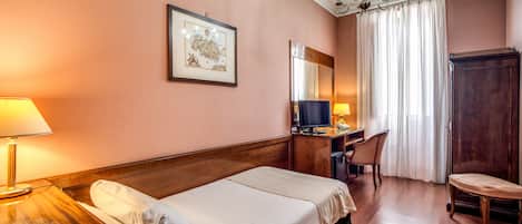 A hotel room with a bed, desk, chair, and a television.