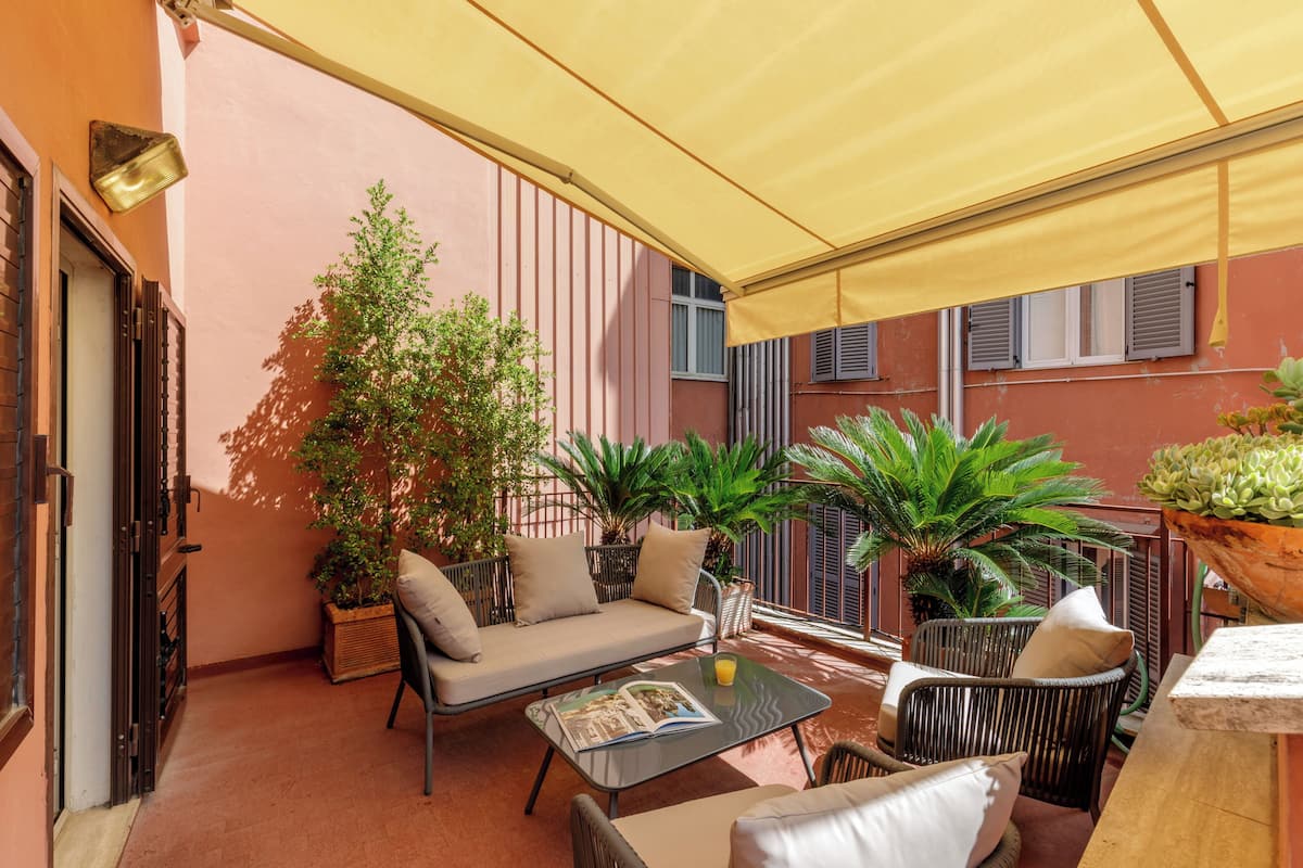 A covered outdoor seating area with a sofa, chairs, and a table, surrounded by potted plants.