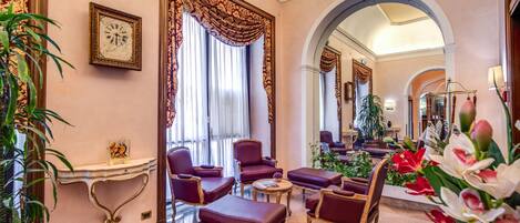 A lobby with a clock, red upholstered chairs, a console table, and a mirror.