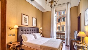 Quarto de hotel com uma cama grande, uma escrivaninha, uma cadeira, uma televisão e varanda com vista para prédios.