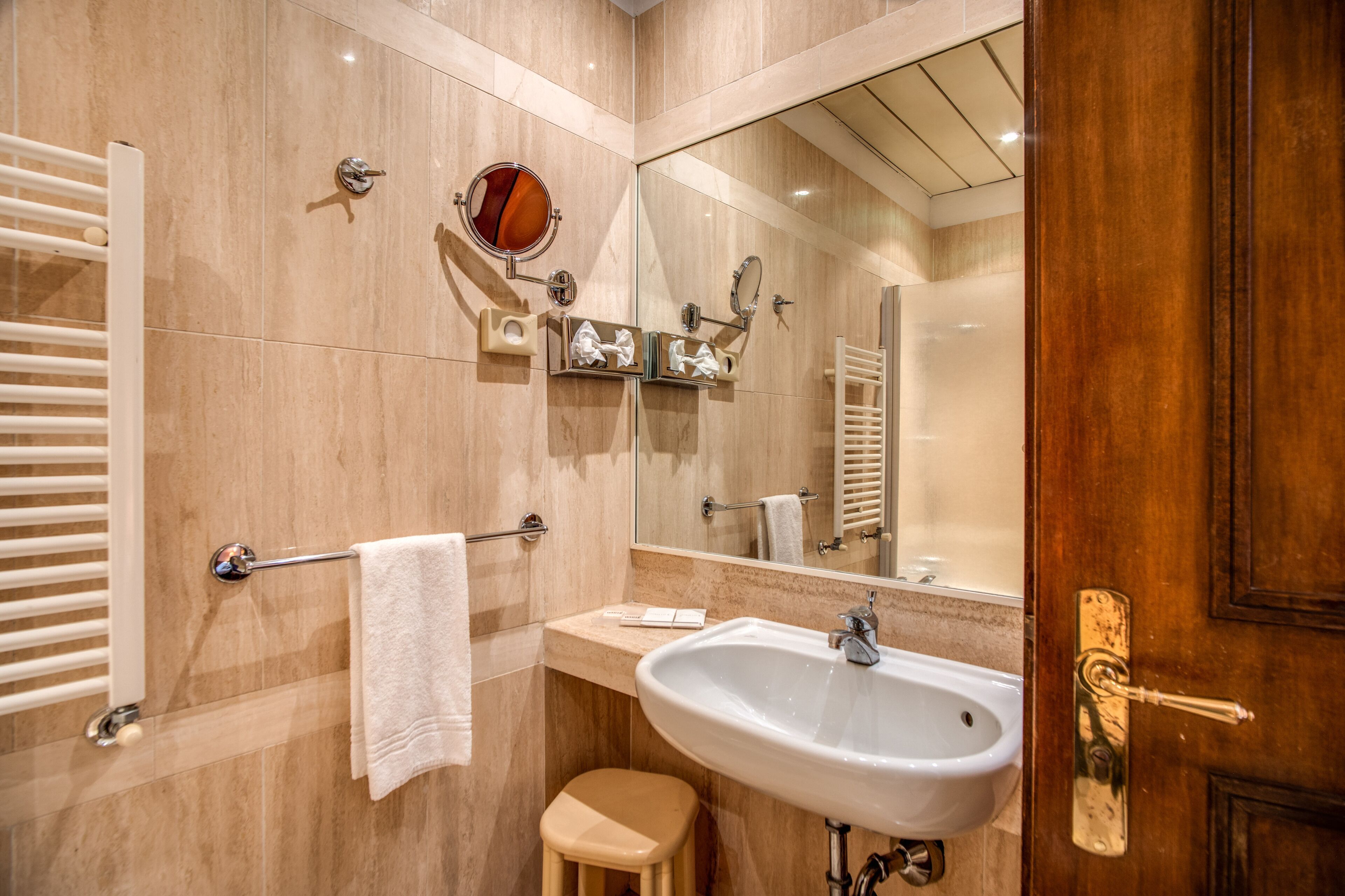 A bathroom with a sink, mirror, towel rack, and a wooden door.