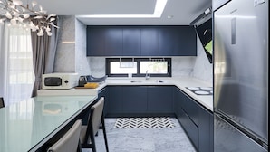 Een moderne keuken met donkere kastjes, een roestvrijstalen koelkast, een magnetron en een glazen eettafel.