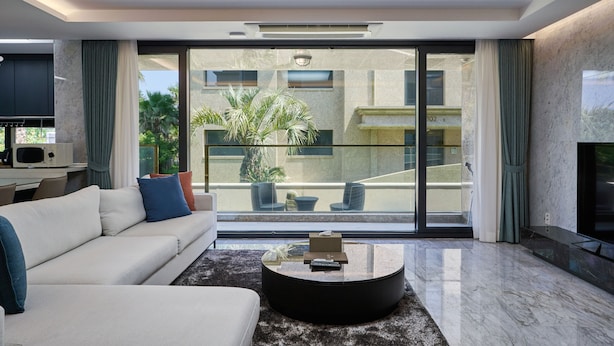 Een moderne woonkamer met een bank, een salontafel en een groot raam met uitzicht op een balkon en palmbomen.