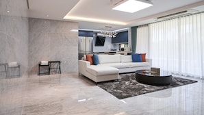 Een moderne woonkamer met een witte hoekbank, een ronde salontafel en een marmeren vloer.