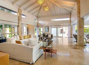 A spacious living area with a large white sofa, a coffee table, and a chandelier. There are large windows providing natural light and a view of the outdoors. - Snrvittinivillas Mng Spacius and Best Loc in Casa de Campo Resorts Gr8 Villa (La Romana)